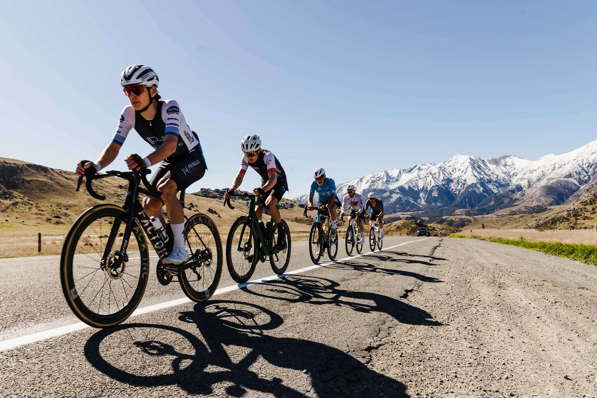Main Divide riders racing through the high country with snow-covered mountains behind them